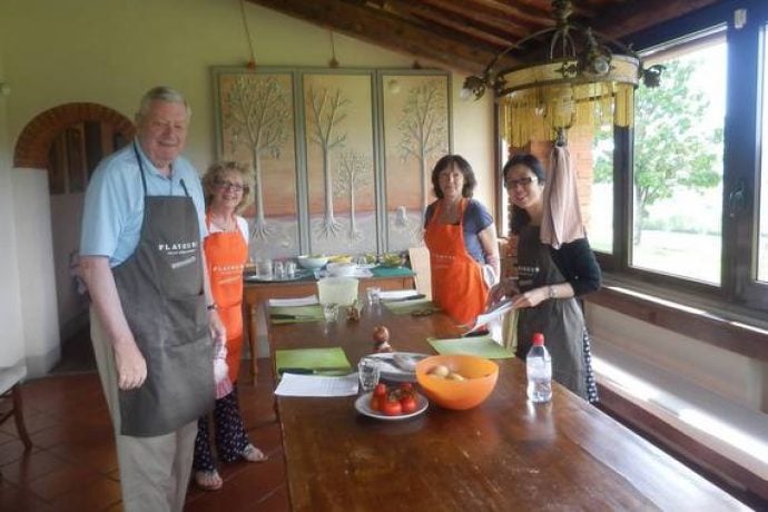 Cooking guests with aprons in Tuscany kitchen during cookery lesson.