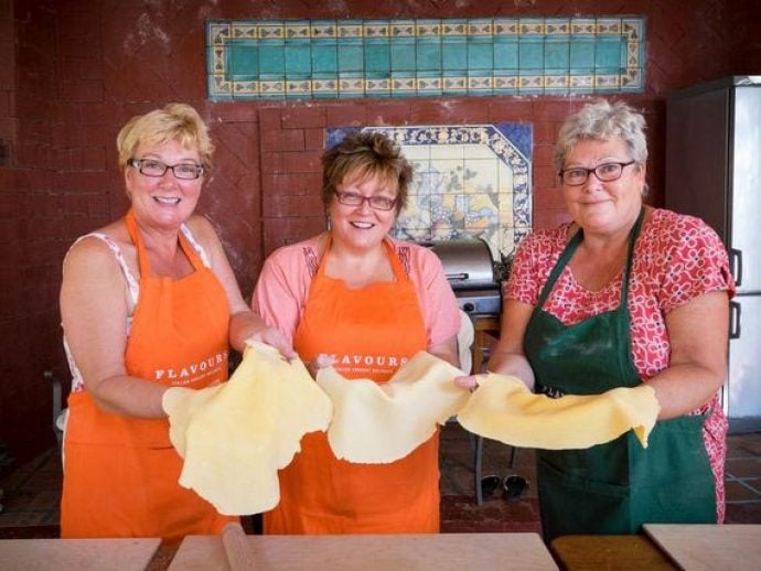 Three ladies in aprons smiling and holding pizza dough