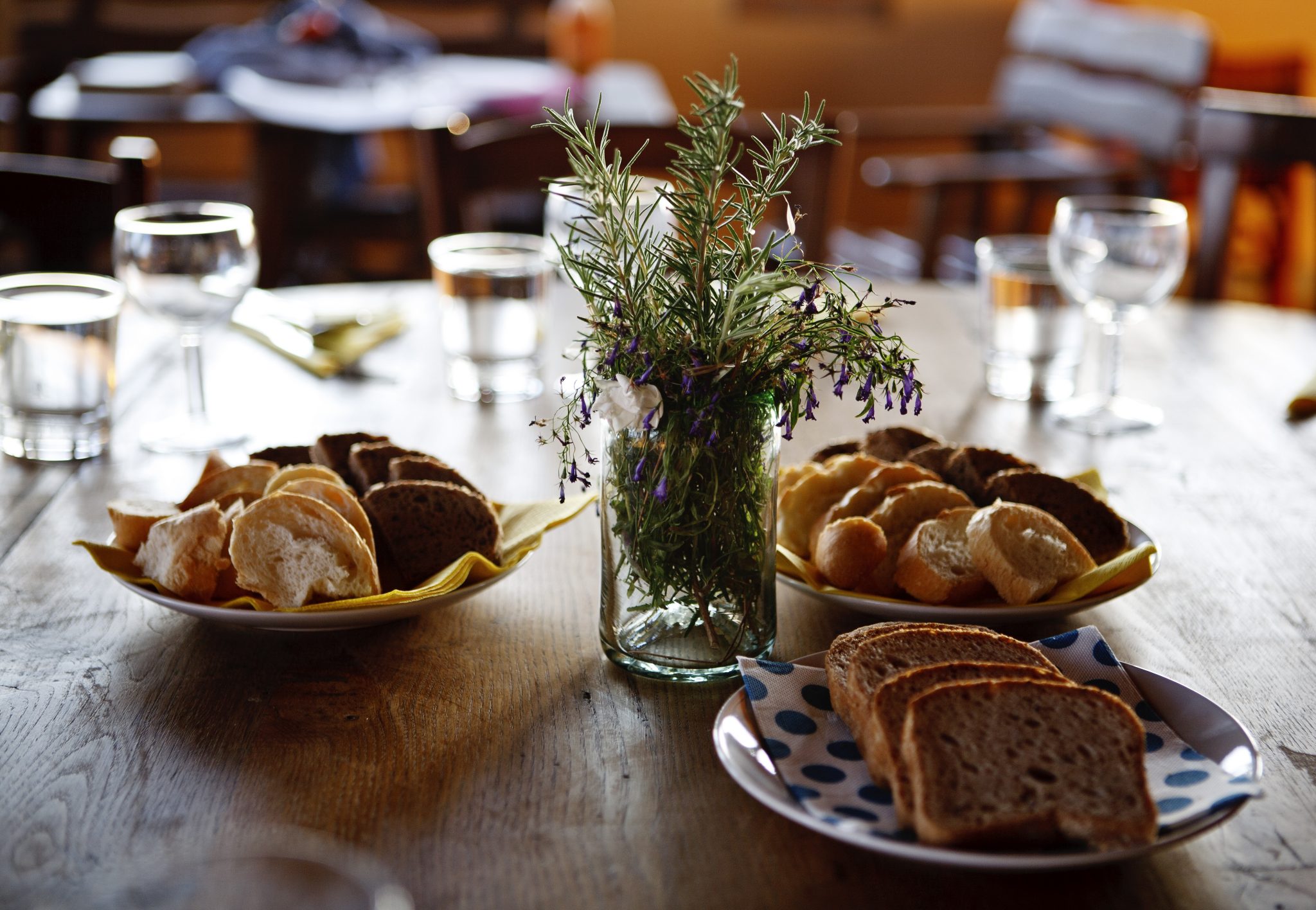 Table laden with plates of different types of breads and wine and water glasses. 